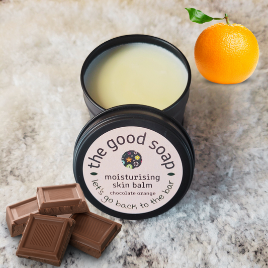 Moisturising skin balm in a black container with an orange and chocolate bars on a textured surface.