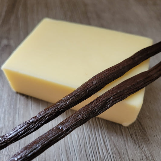 Cocoa Butter and Vanilla solid moisturiser bar, unpackaged, on a wooden background. Decorated with 2 vanilla pods