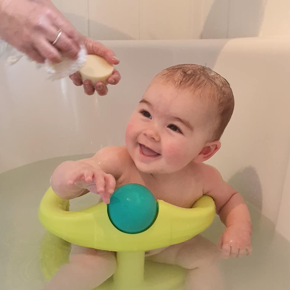 A cute baby in the bath being washed with a natural baby soap bar