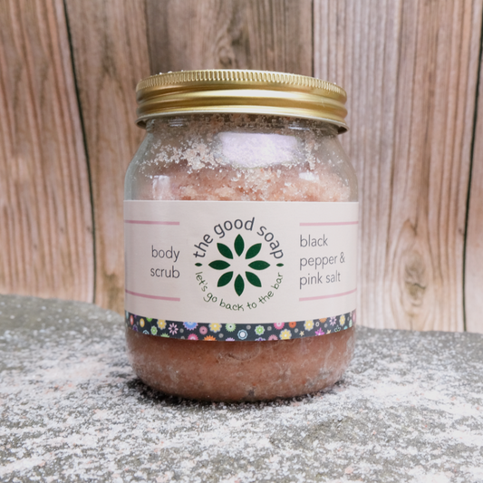 A glass jar of Black Pepper and Pink Salt Body Scrub on a salt background