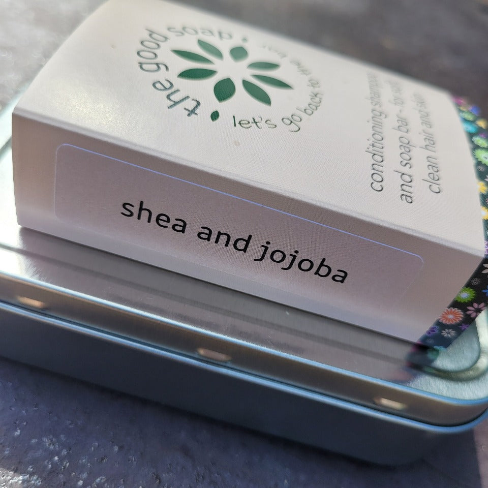 A shea and jojoba soap and shampoo bar on top of a storage tin.
