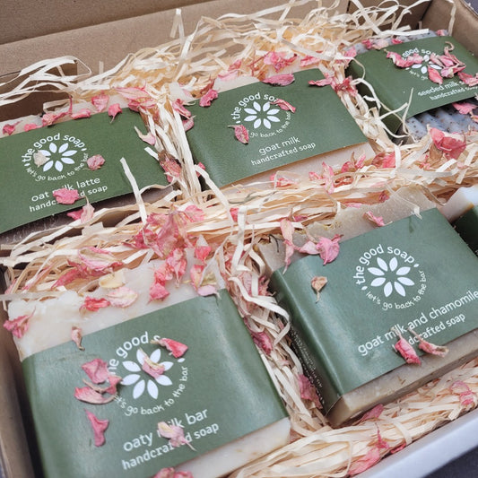 A gift box of 6 artisan milk soaps open. The soaps are lay on straw and are sprinkled in dried rose petals