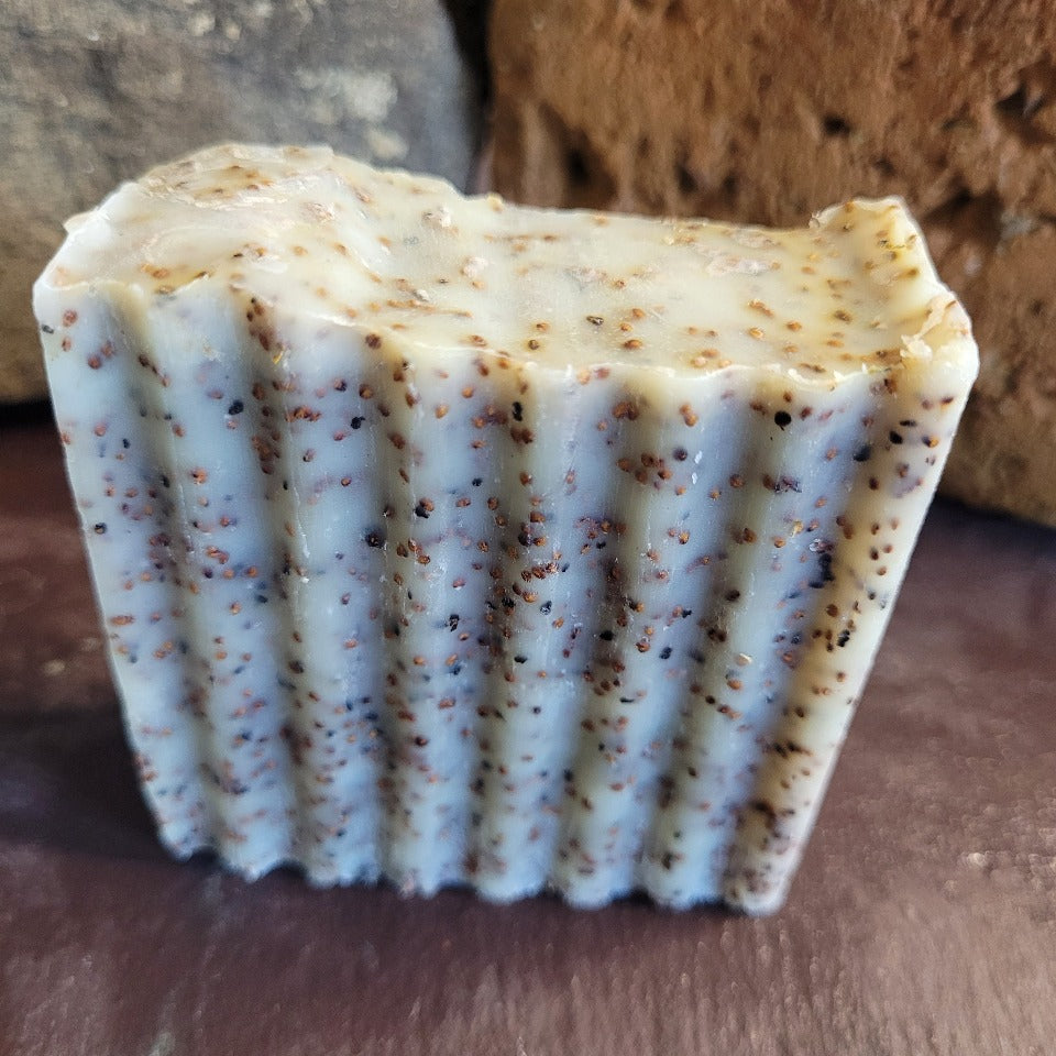 A seeded coconut milk scrub soap in an upright postion, with a brick background