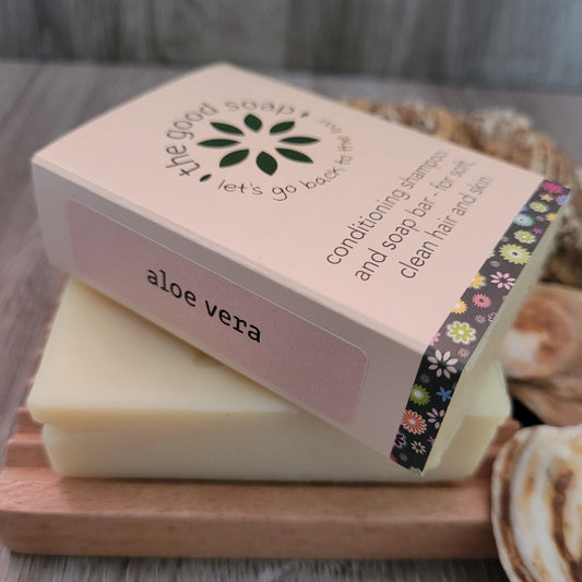 An Aloe Vera soap and shampoo bar in packaging, on a wooden soap dish