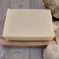 A coconut milk and honey soap bar on a wooden soap dish with shells to decorate.