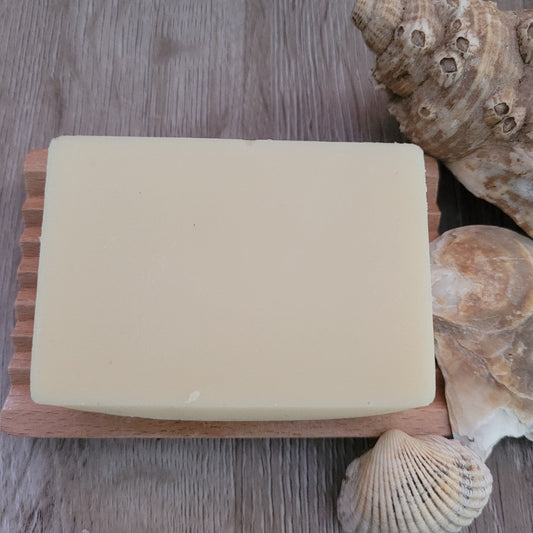 A Shea and Jojoba Soap & Shampoo Bar with no packaging, on a wooden soap dish