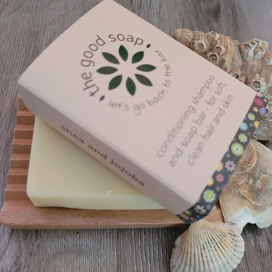 A Shea and Jojoba Soap & Shampoo Bar on a wooden soap dish, on a wooden background decorated with shells