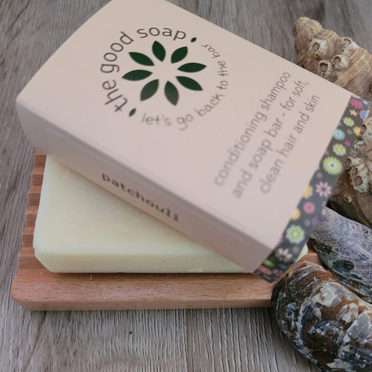 A Patchouli Soap & Shampoo Bar on a soap dish, on a wooden background with some shells for decoration