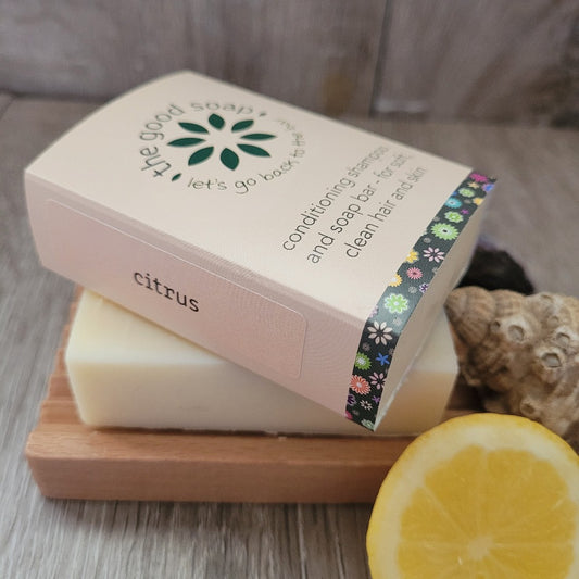 A Citrus Soap & Shampoo Bar in packaging, on a wooden soap dish
