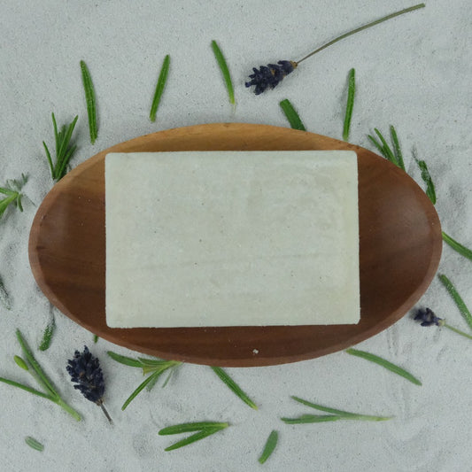 A Lavender Pumice Soap on a wooden soap dish, surrounded by pieces of lavender