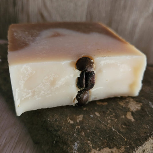 An oat milk lattes soap bar, displaying coffee beans, on a stone background