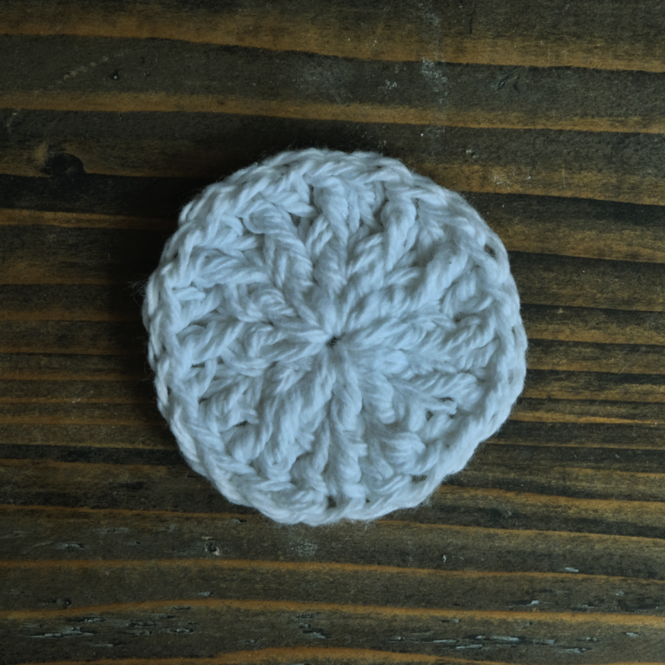 A single crocheted face cleansing disk on a wooden background.