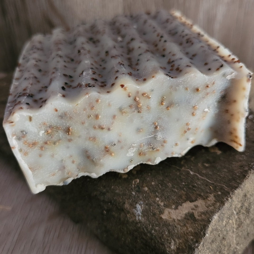 A seeded  scrub coconut milk soap on a stone and wood background