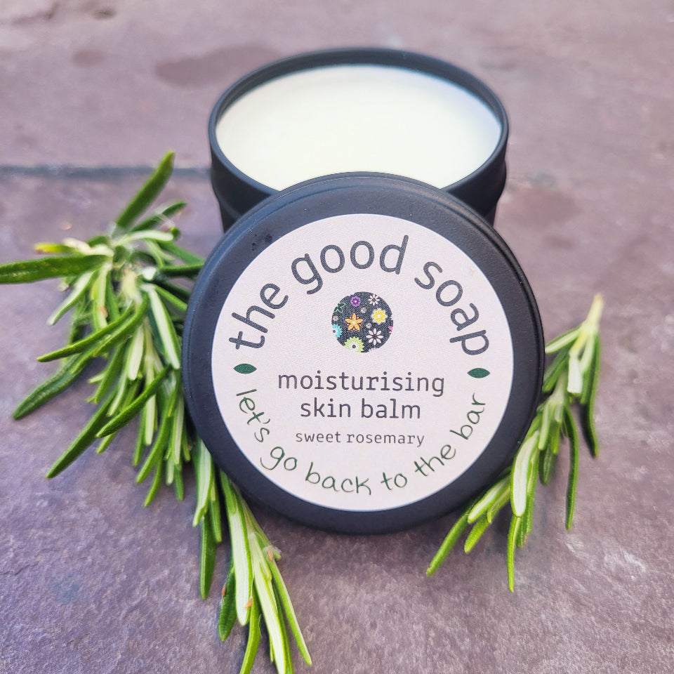 Moisturising skin balm container with rosemary leaves on a stone surface