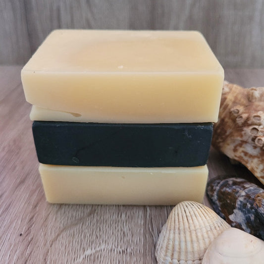 A stack of 3 unpackaged natural soap bars on a wooden background, with shells for decoration