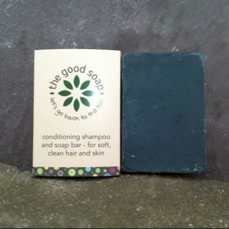 2 activated charcoal natural soap and shampoo bars standing upright on stone background, one in packaging, one unpackaged