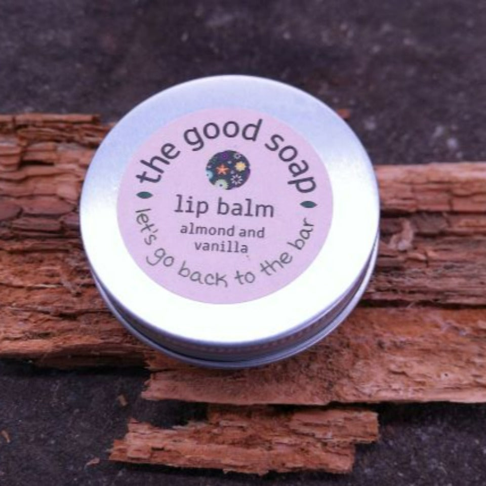 Almond and vanilla lip balm in a metal screwtop tin on a piece o driftwood