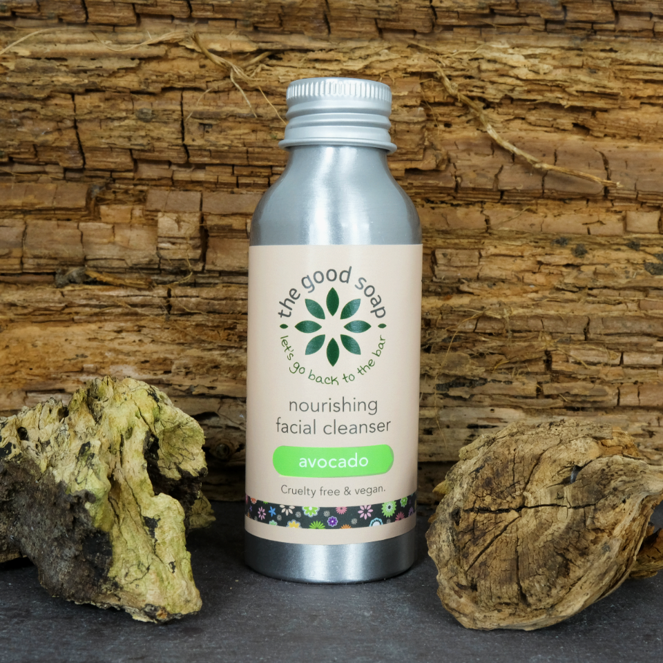 A bottle of avocado facial cleanser. Cleanser is in an aluminium bottle and is displayed on a wooden background.
