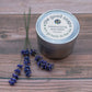 A tin of Lavender Skin Balm on a wooden background, next to the tin are some sprigs of lavender
