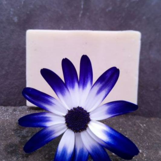 The Good Soap natural deodorant bar in floral scent. The bar is on a slate background and is deorated with a pretty blue flower