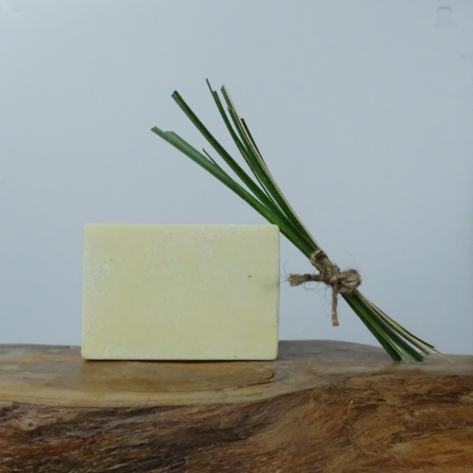 A natural solid deodorant bar on a wooden background, with a sprig of lemongrass