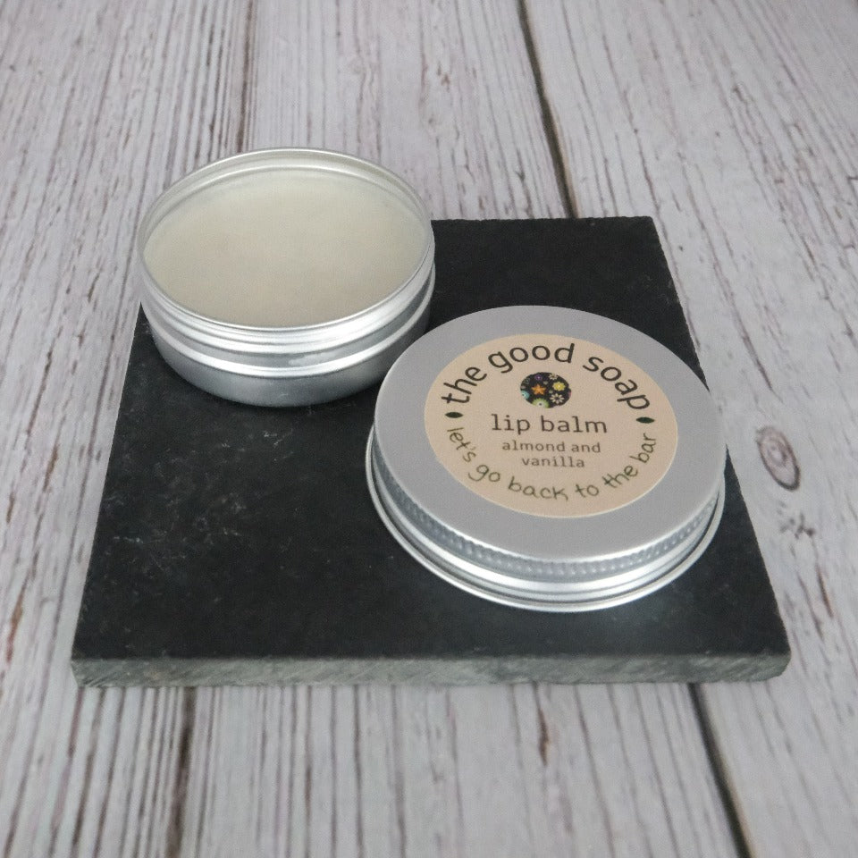 An open tin of almond and vanilla lip balm on a slate and wooden background