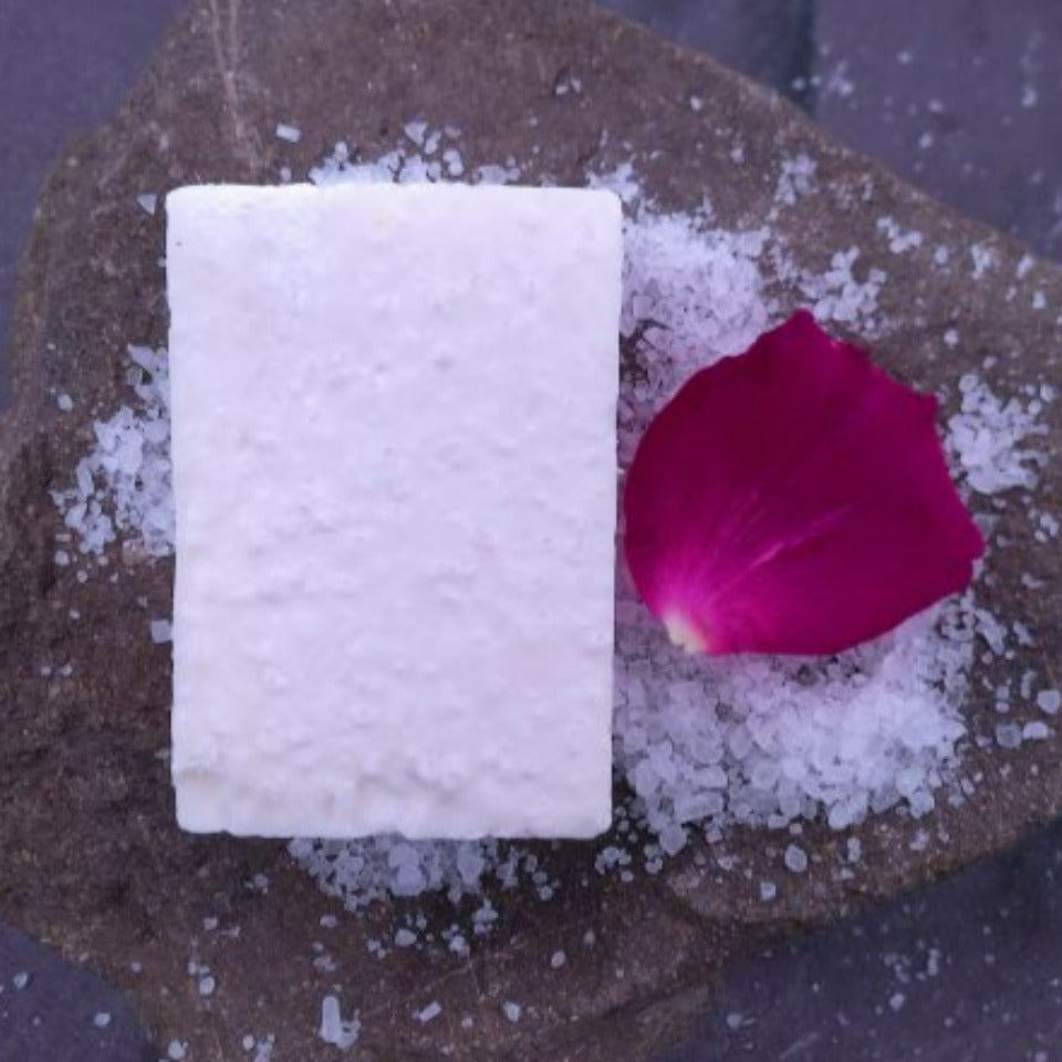 A Rose Salt Soap on a stone background, with a pink rose petal and sprinkled with sea salt