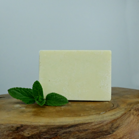 A natural spearmint and lemon solid deodorant bar on a wooden background, with a sprig of spearmint