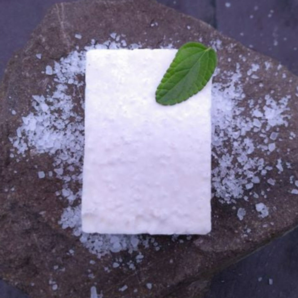 A Peppermint and Tea Tree Salt Soap on a stone background, decorated by a mint leaf and sea salt