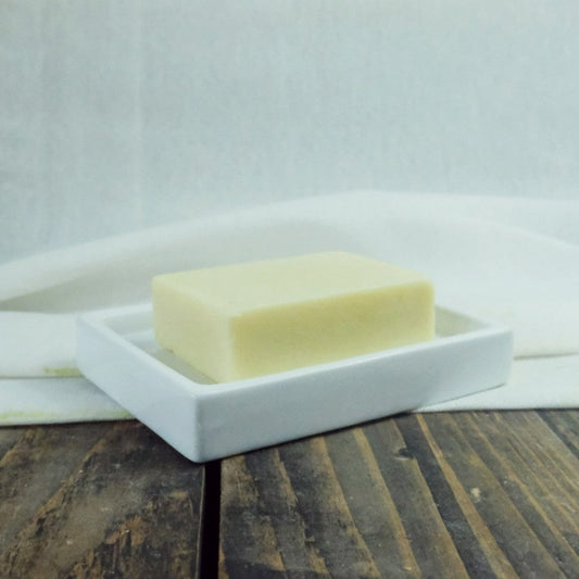 A hemp seed oil solid moistiriser bar on a ceramic dish. The bar is displayed on a wood and muslin background