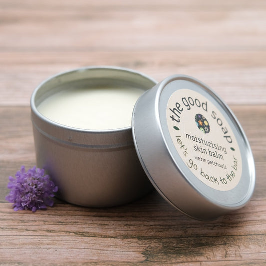 An open tin of Warm Patchouli Skin Balm on a wooden background, with a pretty patchouli flower