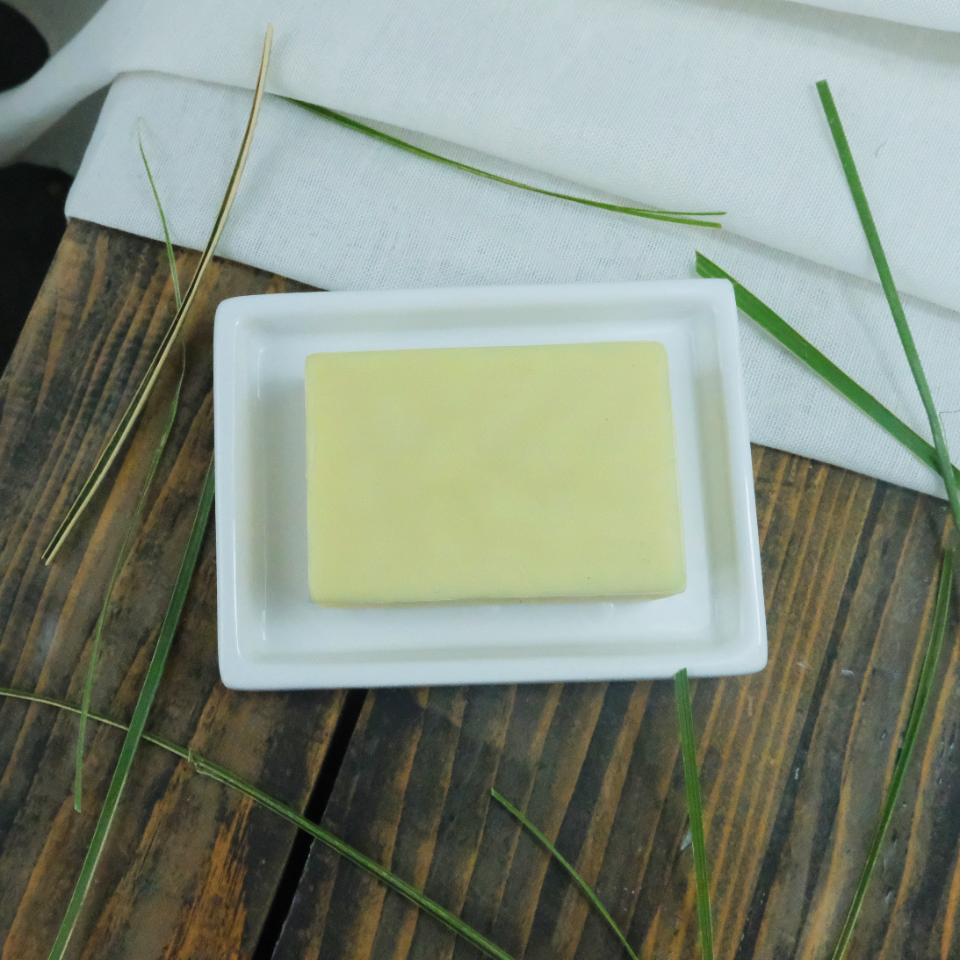 A Lemongrass solid moisturiser bar on a ceramic dish, surronded by strands of lemongrass