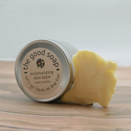 A tin of Warm Vanilla Skin Balm on a wooden background with a chunk of cocoa butter